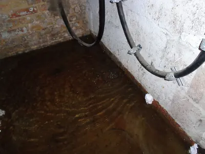 Standing water on a basement floor along a painted brick wall