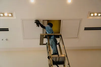 Worker on a ladder reaching into a ceiling access panel